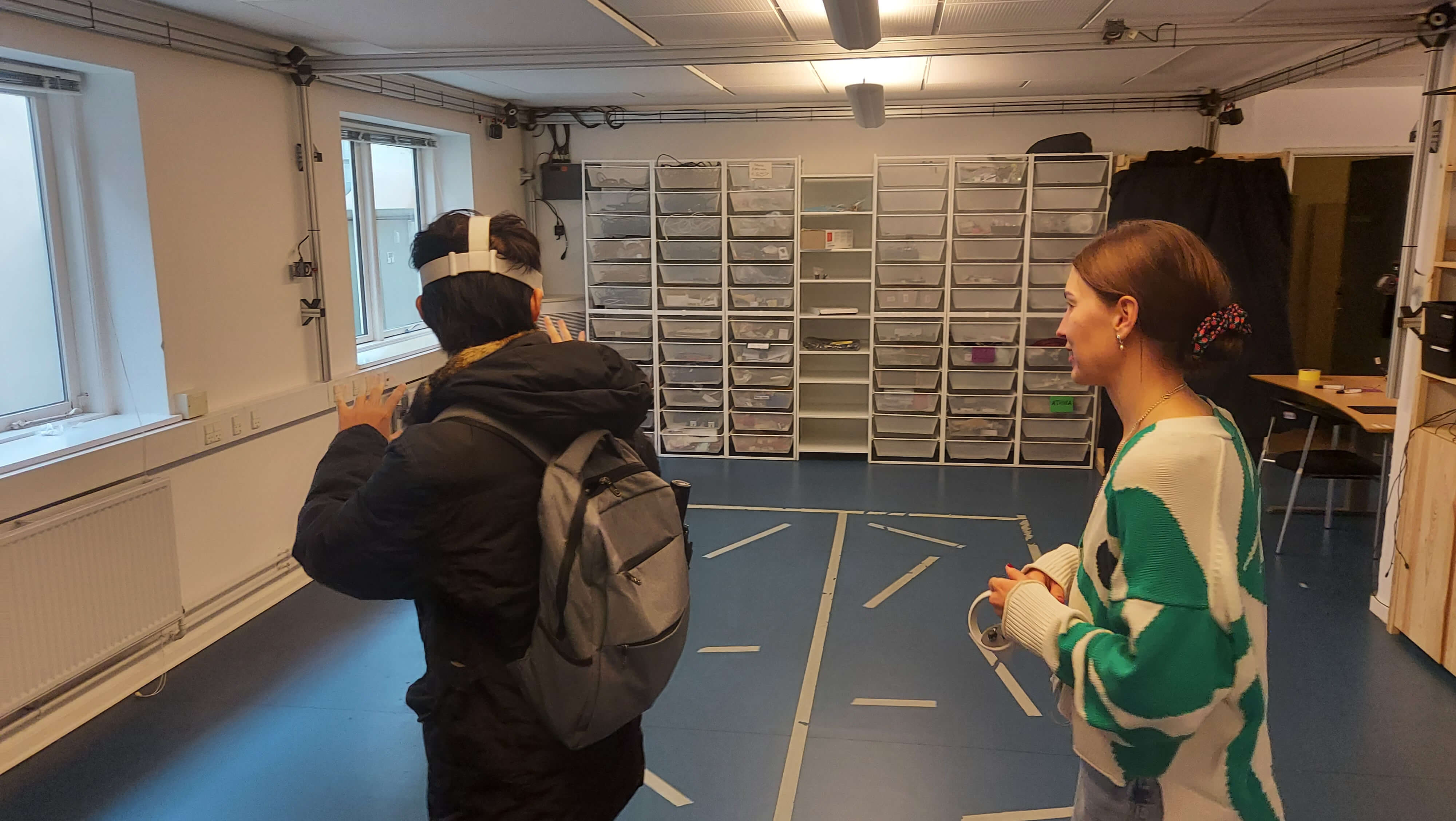 One person using VR equipment in the presence lab, another person by their side